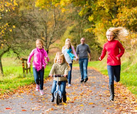 Isä, äiti ja neljä eri-ikäistä tyttöä ulkoilevat syksyisessä puistossa.