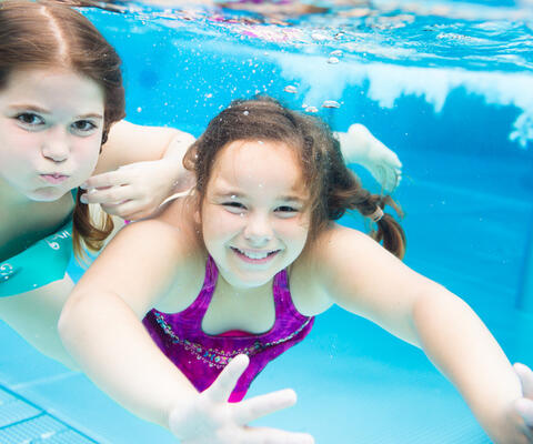 Kaksi tyttöä sukeltaa uimahallissa.