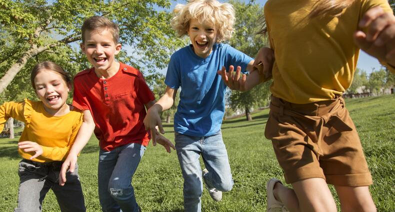 Lapset juoksevat kesällä nurmikolla.