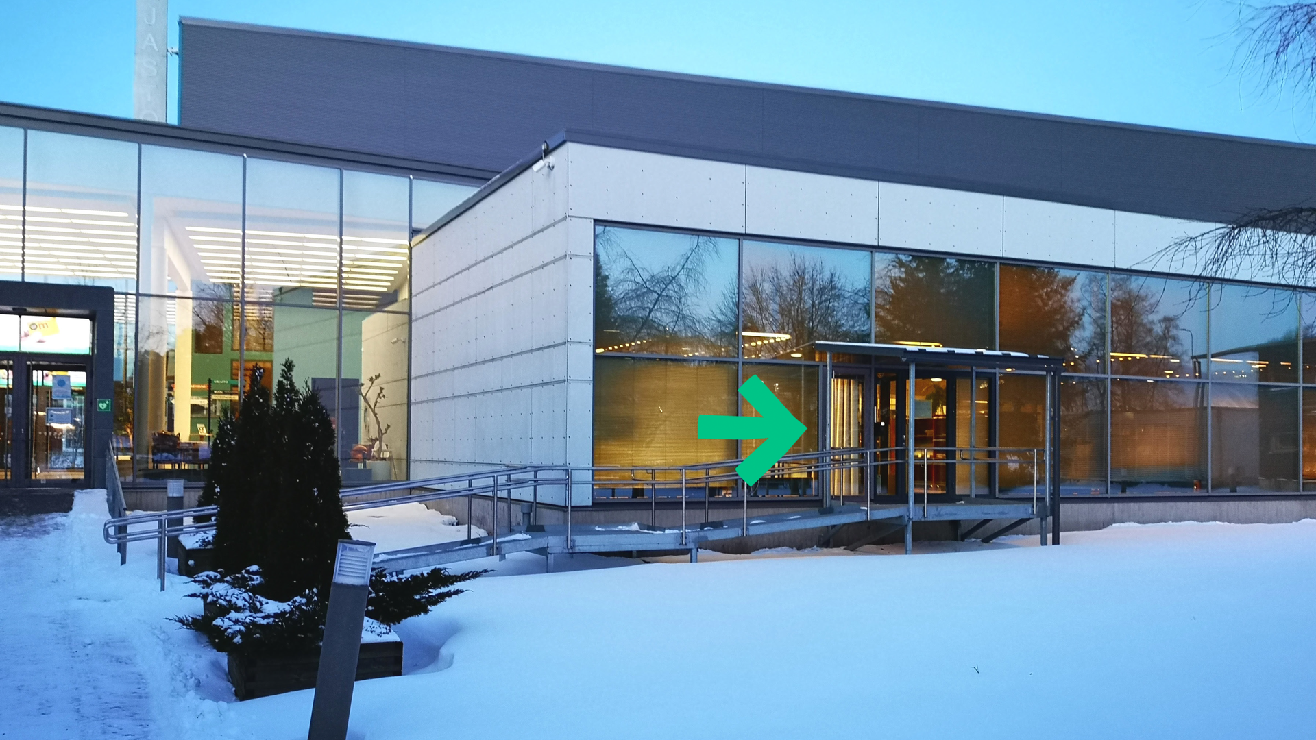Raision Kirjastotalon talvella. Kuvassa vihreä nuoli osoittaa uutta sisäänpääsyä omatoimialueelle.