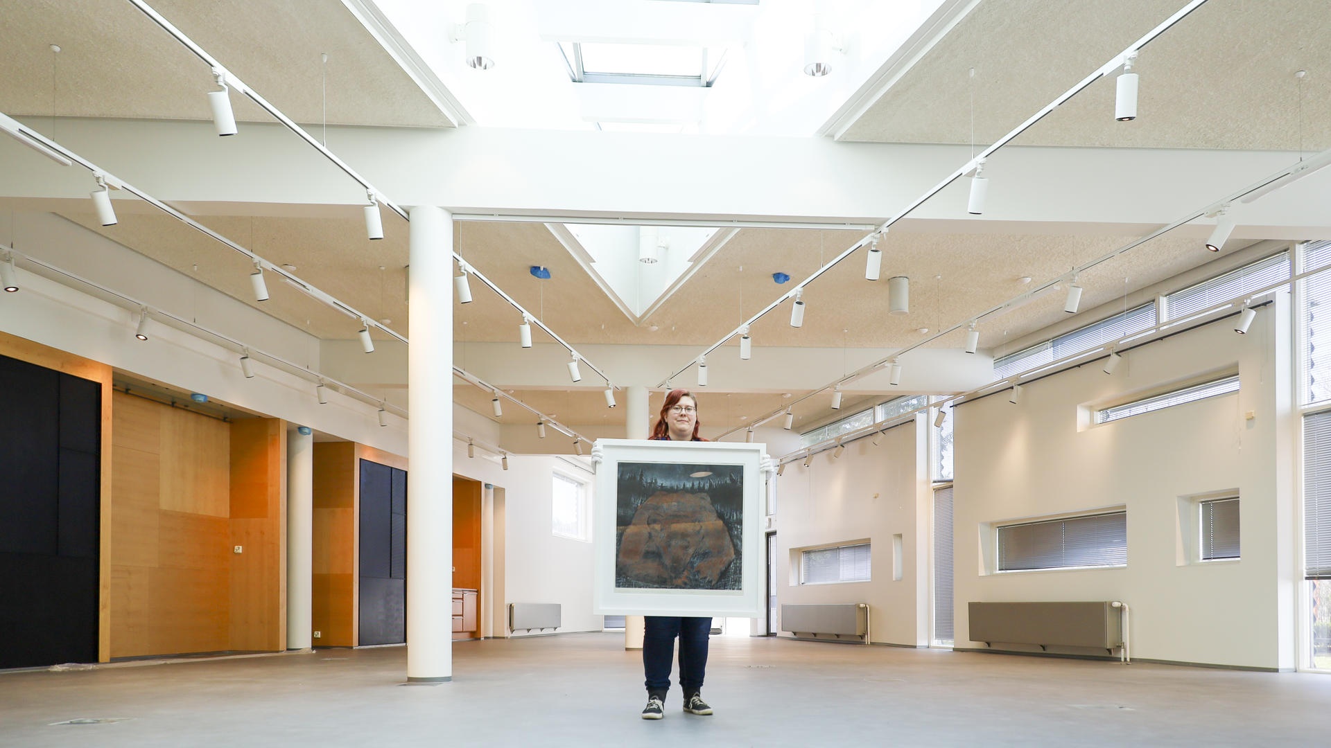 Kirsi Leimu pitää uusissa museotiloissa käsissään taideteosta näyttelystä Linnunradan alla – Eläimiä taiteessa ja taruissa.
