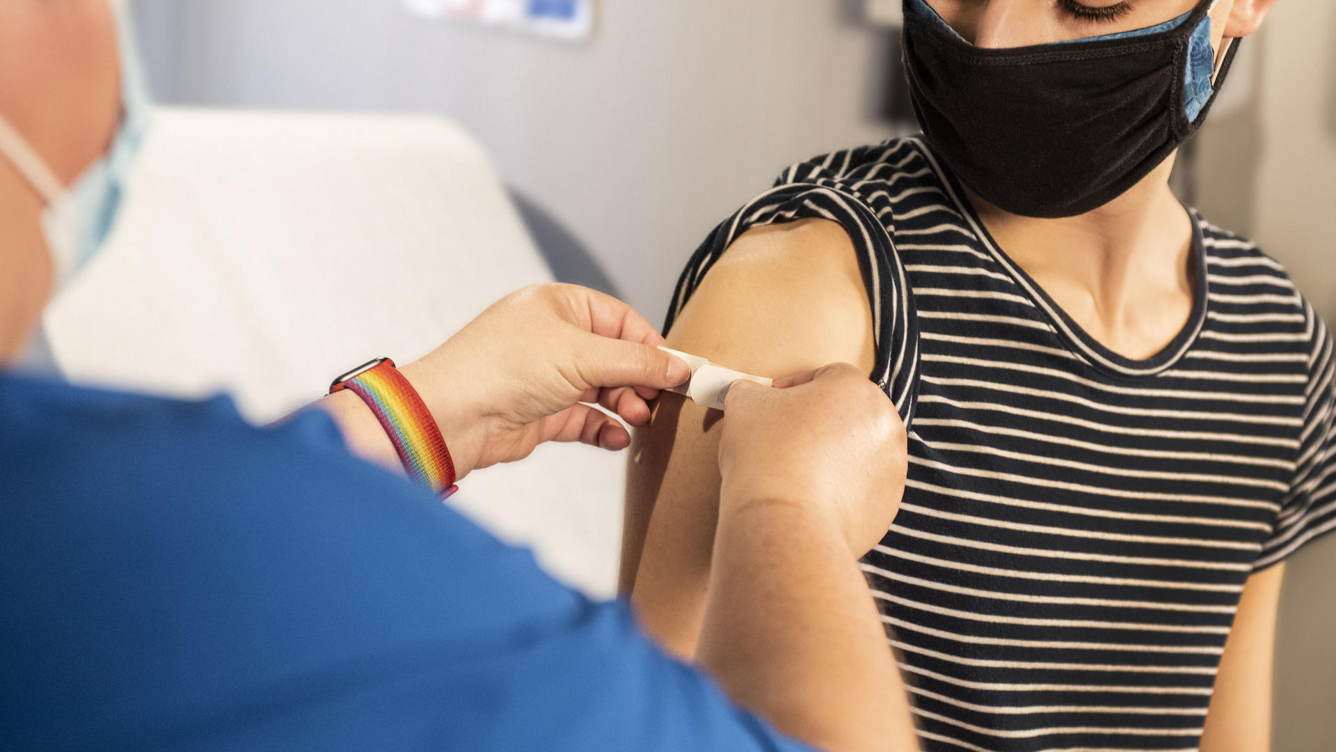 Hoitaja laittaa nuorelle laastaria käsivarteen rokotuksen jälkeen