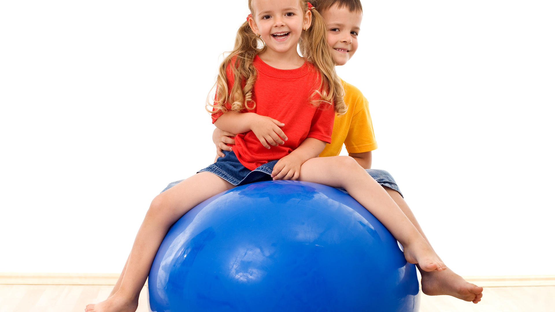 Kaksi lasta istuu sinisen jumppapallon päällä.