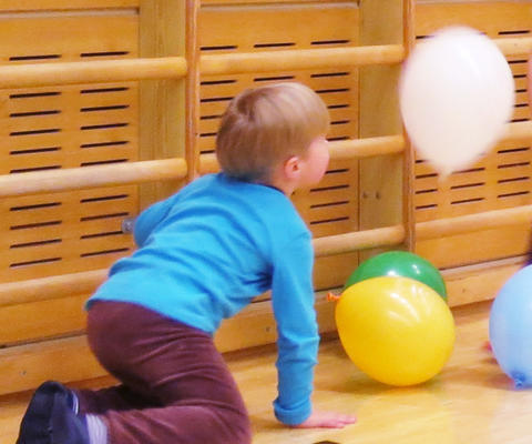 Pieni lapsi liikuntasalin lattialla leikkimässä ilmapalloilla.