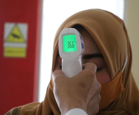 Lääkäri mittaa kuumetta hijabiin pukeutuneelta naiselta.