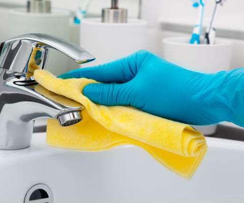 Käsi pyyhkii vesihanaa keltaisella siivousliinalla.