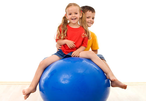 Kaksi lasta istuu sinisen jumppapallon päällä.
