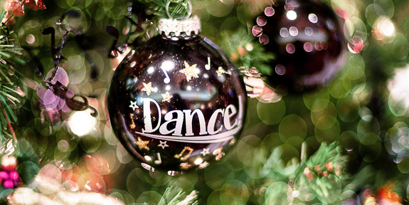 Lähinäkymä joulukuusen oksasta, jossa roikkuu joulupallo. Koristeessa lukee Dance.