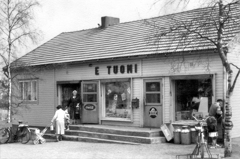 Raisiolaista historiaa, Tuomen kauppa Vanha mustavalkoinen kuva, jossa matala puurakennus. Rakennuksen ulkopuolella ihmisiä.